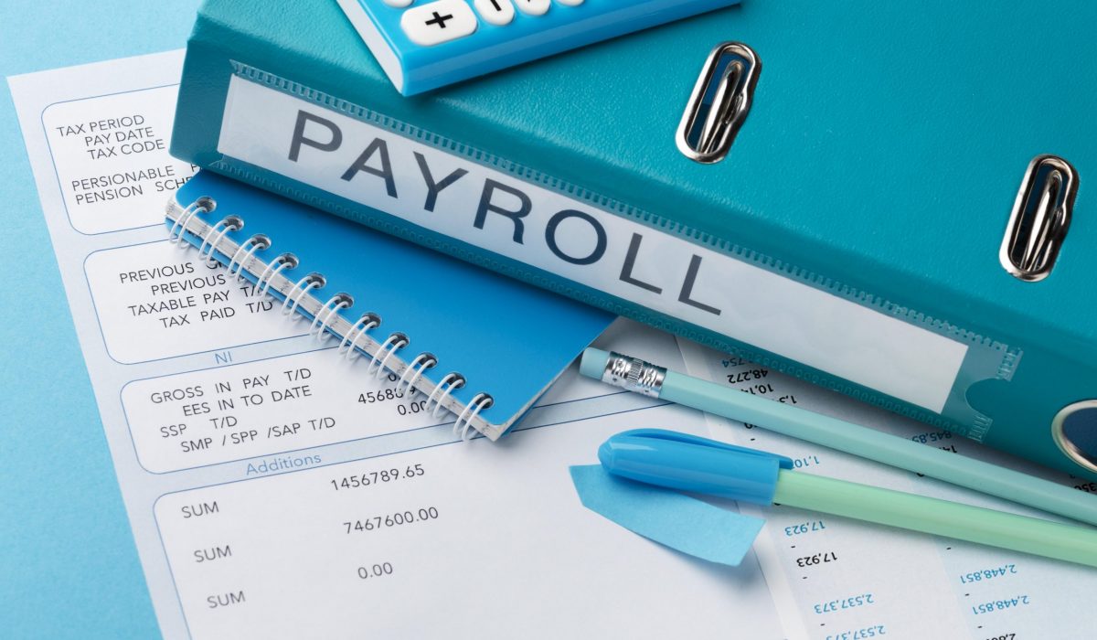 Payroll documents, calculator, and blue binder labeled 'PAYROLL' on a desk, highlighting the benefits of outsourcing payroll for SMEs in Malaysia to reduce administrative burden and improve efficiency.